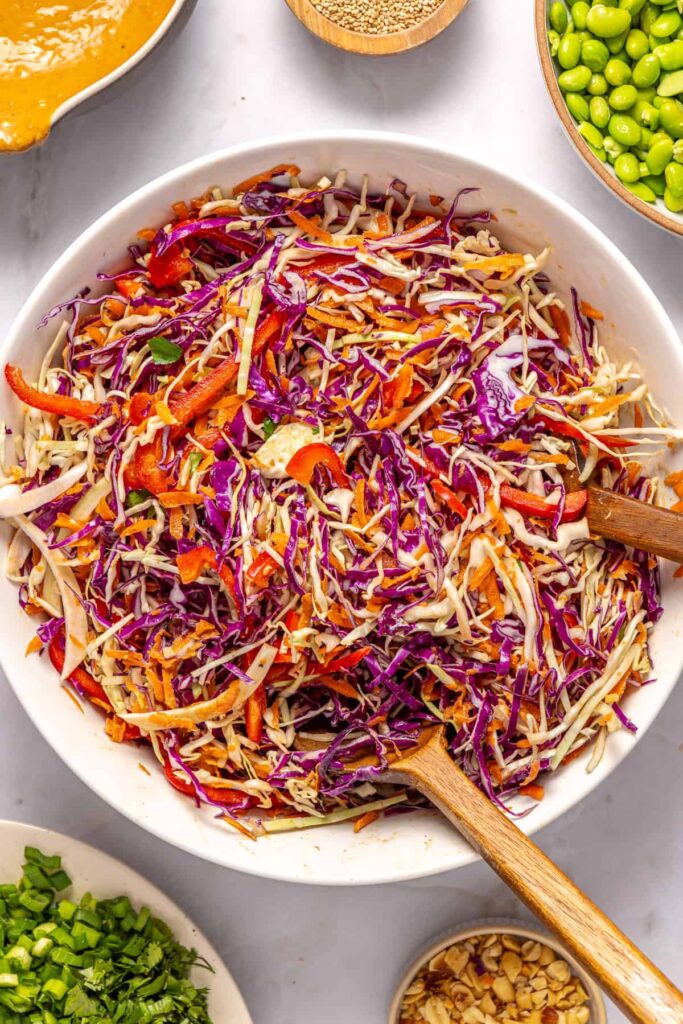 Tossing cabbage, bell peppers, and carrots with peanut dressing for crunchy peanut cabbage salad
