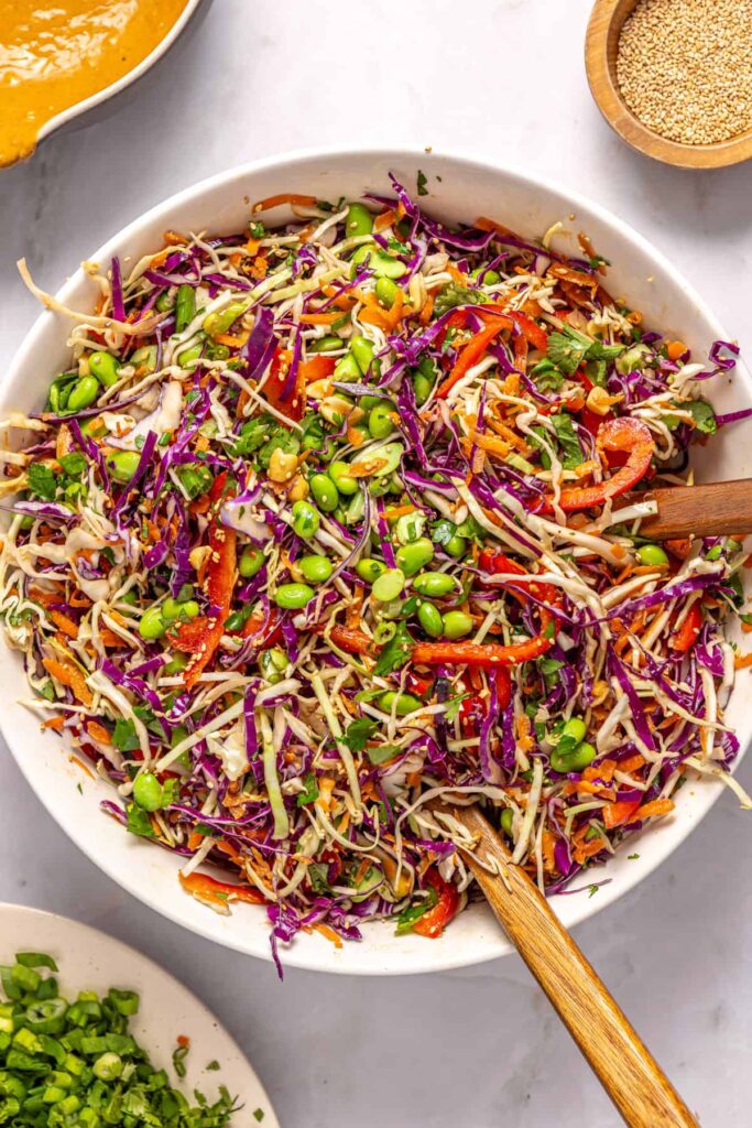 Adding edamame, green onions, cilantro, and peanuts to crunchy peanut cabbage salad