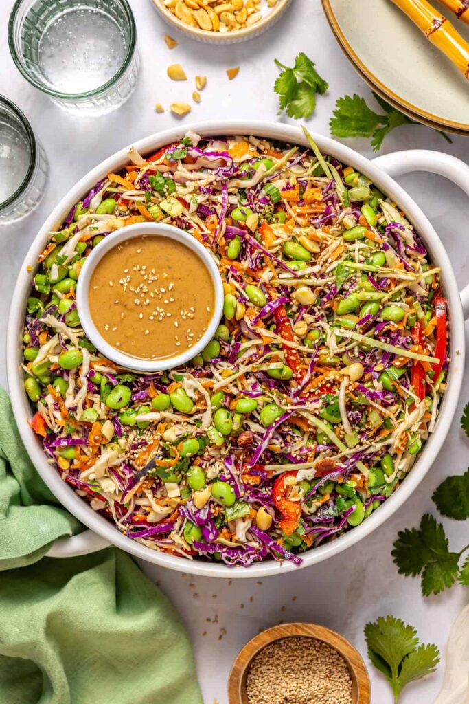 Overhead shot of crunchy peanut cabbage salad in white serving bowl with sesame peanut dressing and sesame seeds