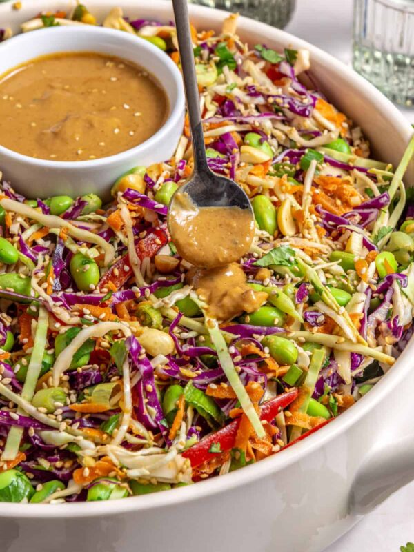Drizzling sesame peanut dressing over crunchy peanut cabbage salad