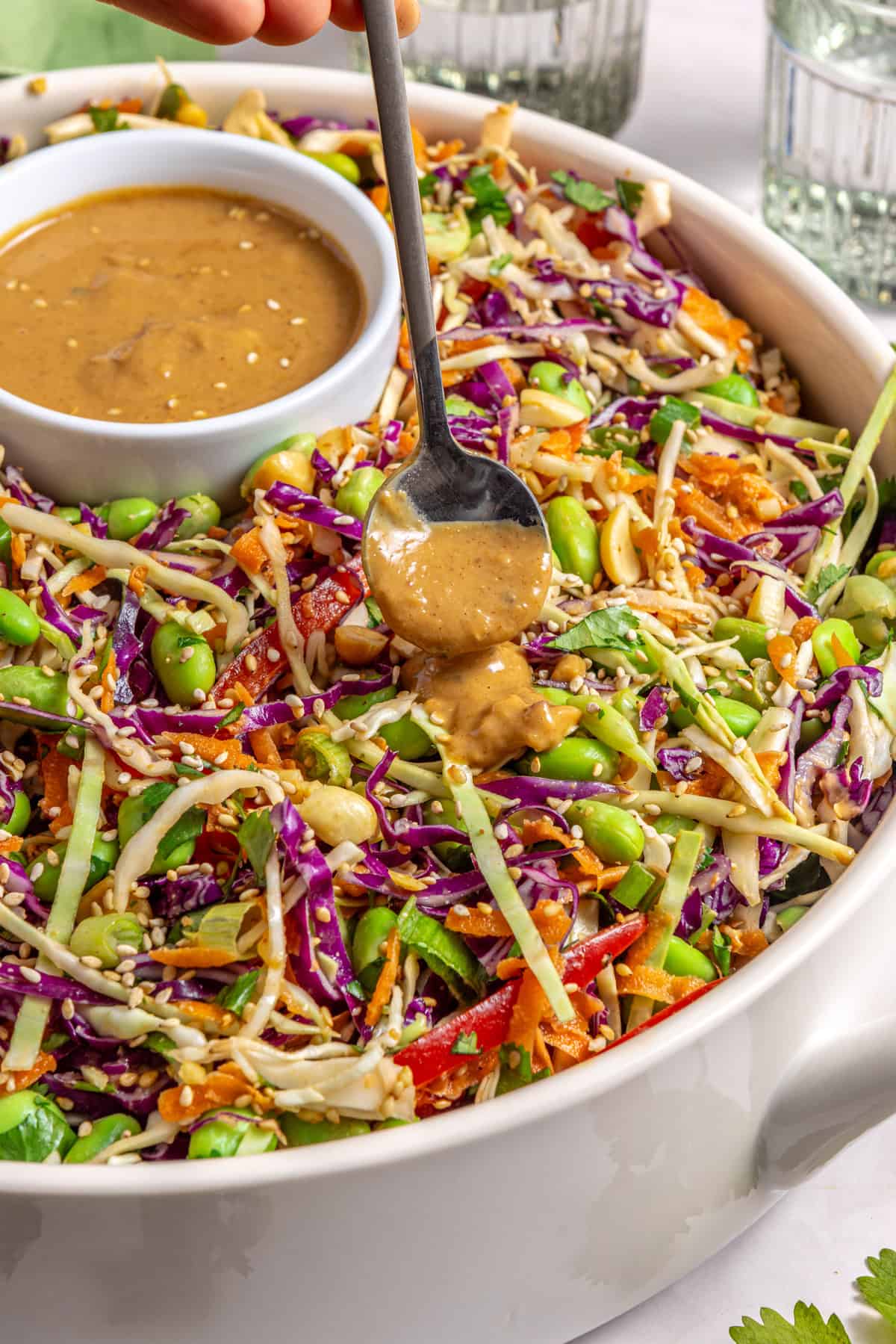 Drizzling sesame peanut dressing over crunchy peanut cabbage salad