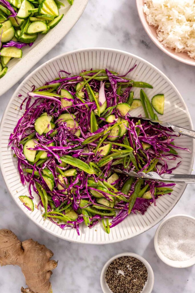 Tossing snap peas, cabbage and cucumber with dressing