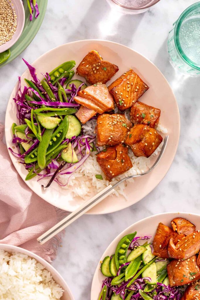Overhead view of air fryer salmon bites with snap pea slaw and rice on a plate with a fork and napkin