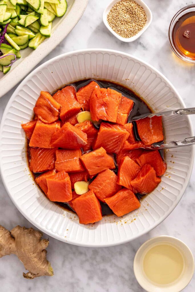 using tongs to toss salmon in marinade for flavorful salmon bites