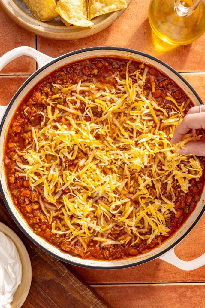 Topping chili skillet with cheddar cheese before melting