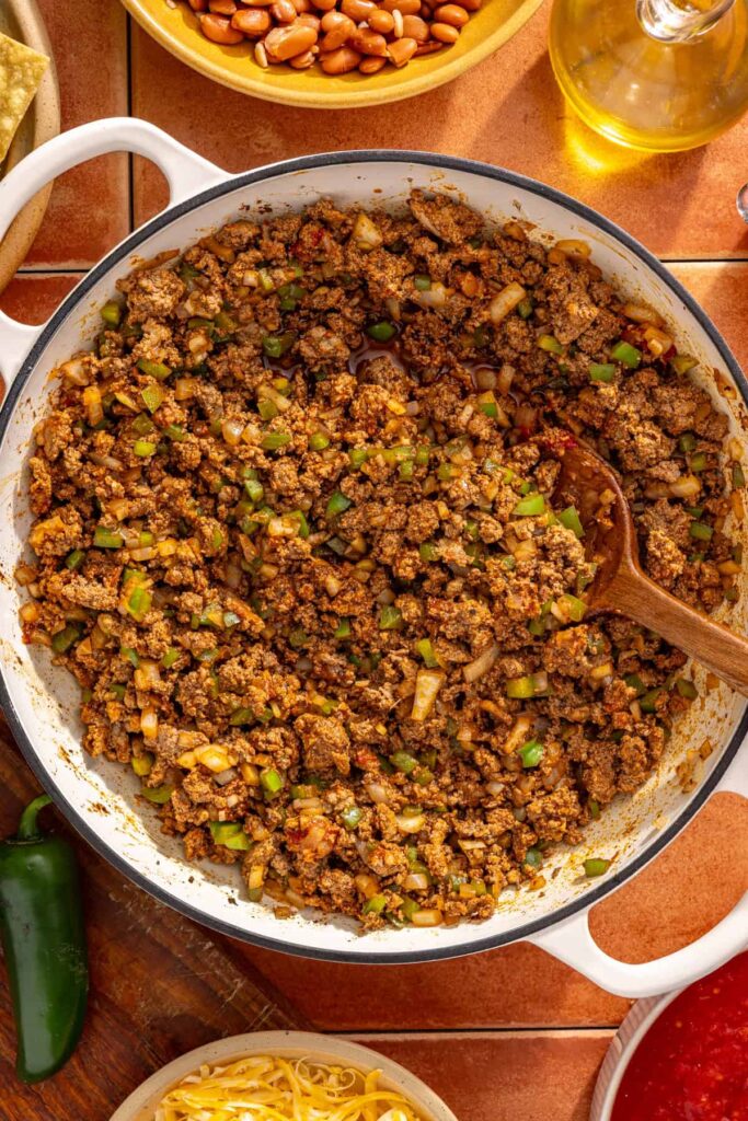 Cooking tomato paste into seasoned meat mixture for chili