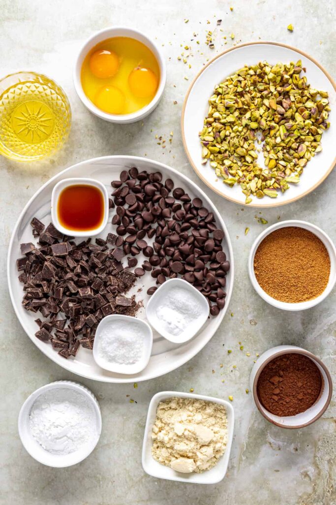 Overhead ingredients for gluten-free pistachio brownies including cocoa powder, pistachios, and dark chocolate
