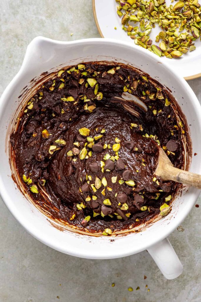 Folding chocolate chips and chopped pistachios into brownie batter
