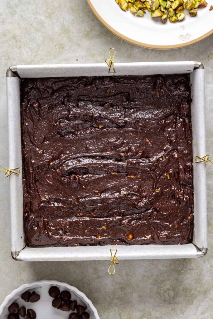 Pistachio brownie batter spread in parchment lined baking pan