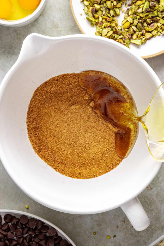 pouring avocado oil into a mixing bowl with coconut sugar for fudgy pistachio brownies