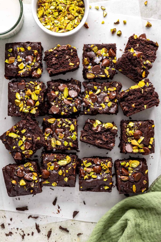 Pistachio brownies on parchment with bowl of pistachios and glass of milk