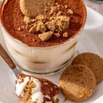 High-protein tiramisu cups served on a plate with cookies and a spoonful of creamy tiramisu