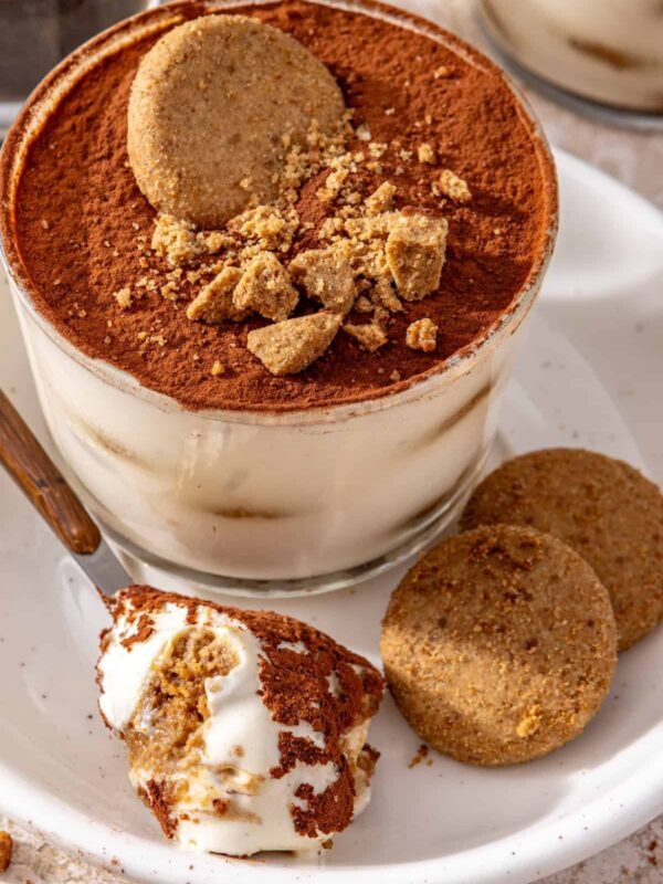 High-protein tiramisu cups served on a plate with cookies and a spoonful of creamy tiramisu