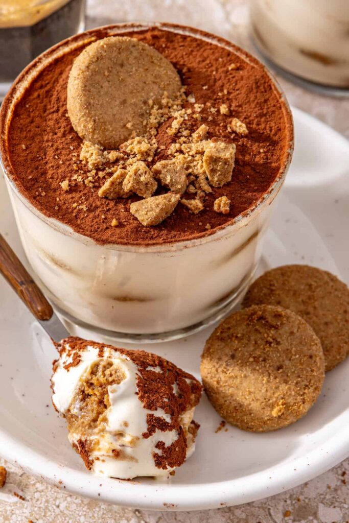 High-protein tiramisu cups served on a plate with cookies and a spoonful of creamy tiramisu