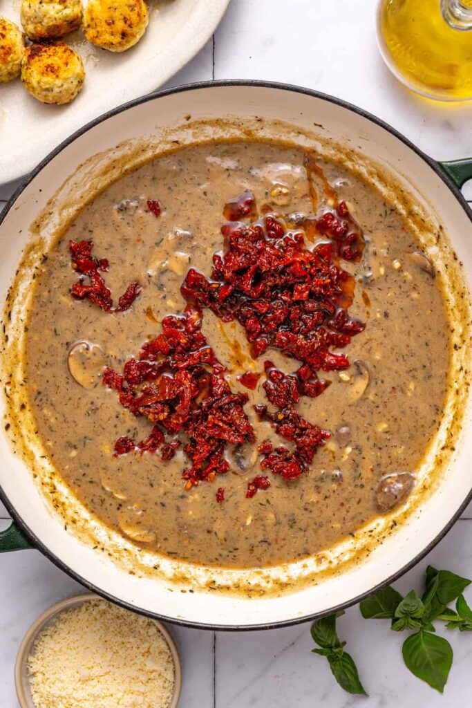 adding sun-dried tomatoes into creamy sauce for marry me chicken meatballs