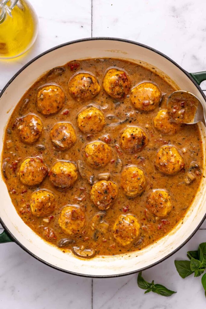 Adding chicken meatballs back into skillet with creamy sauce before baking