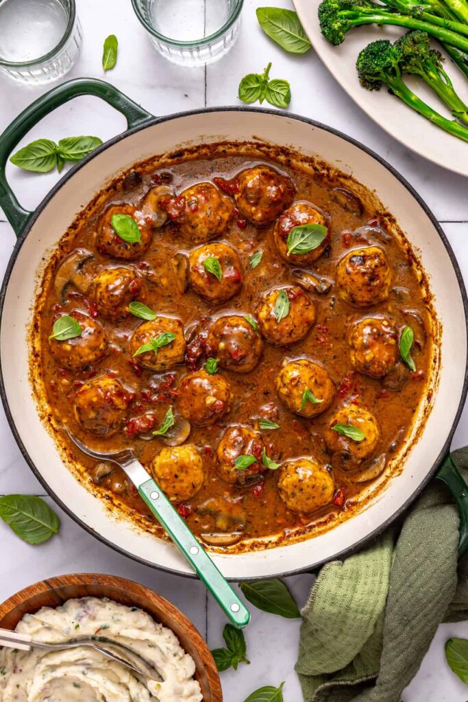 Creamy sun-dried tomato chicken meatballs with basil garnish on a set table