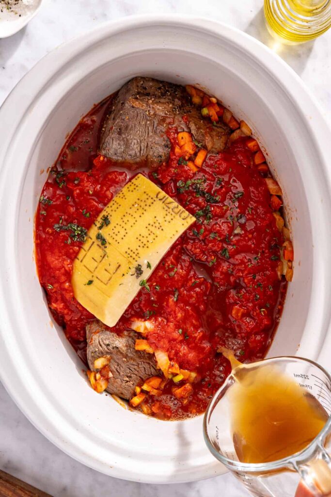 Assembling slow cooker short rib ragu with broth tomatoes and herbs
