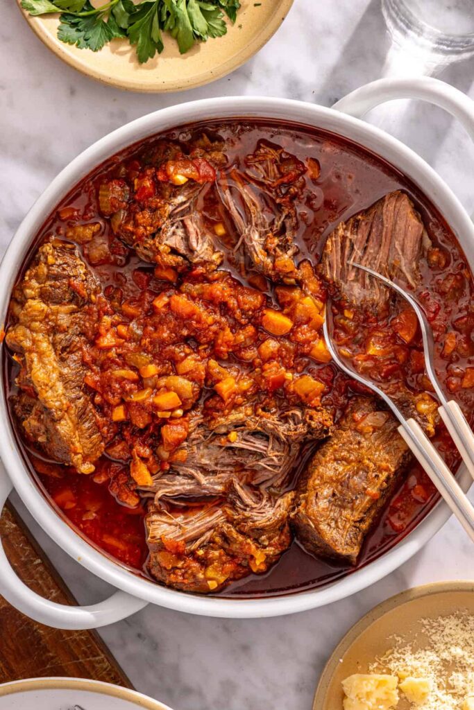 Forks pulling apart beef for slow cooker short rib ragu