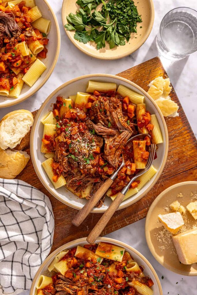 Overhead view of short rib ragu pasta with bread and fresh herbs