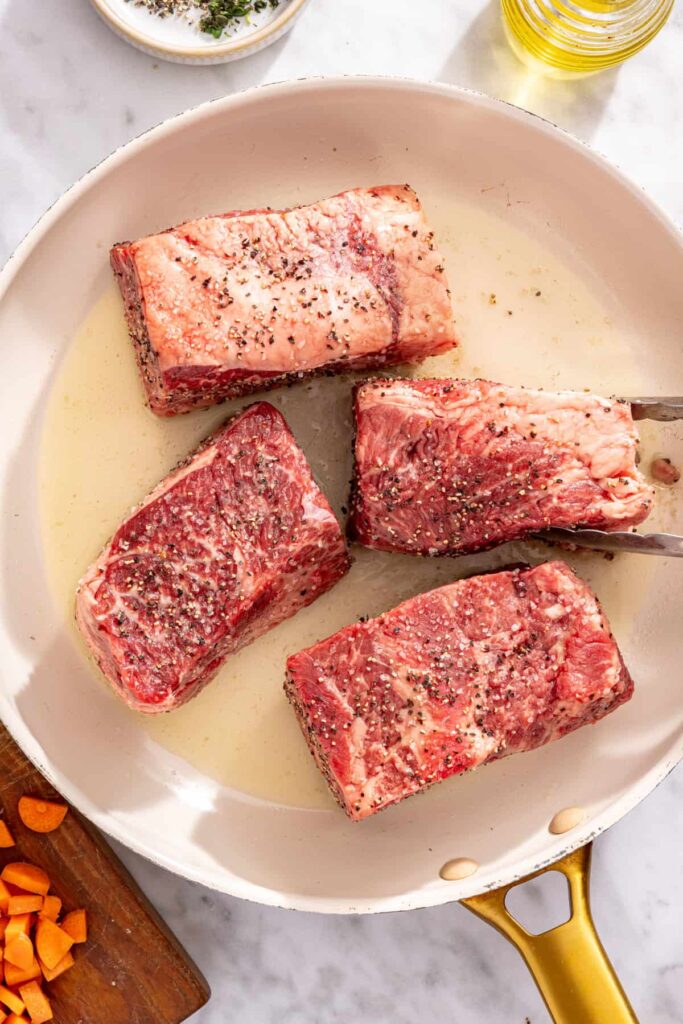 Short ribs searing in a pan until browned for slow cooker short rib ragu