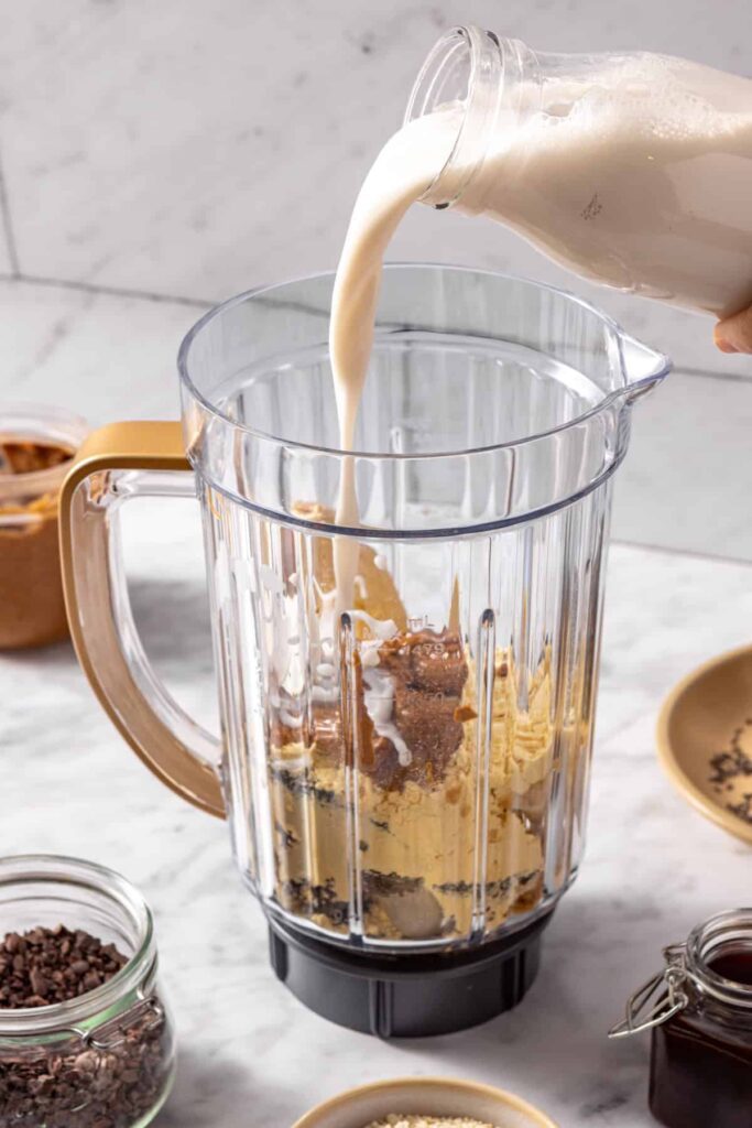 Pouring coconut milk into blender for a healthy dessert smoothie