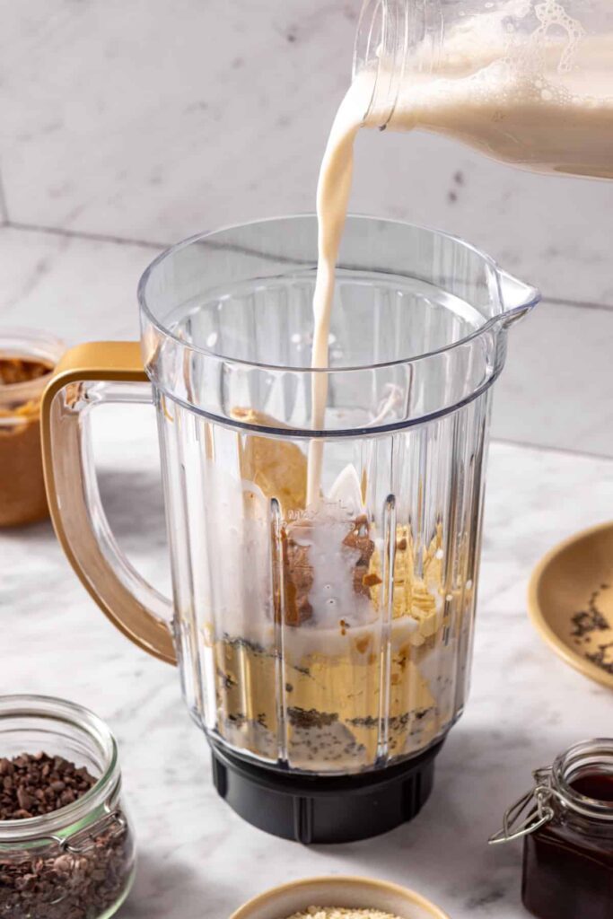 Action shot of milk being poured into smoothie blender with banana and almond butter