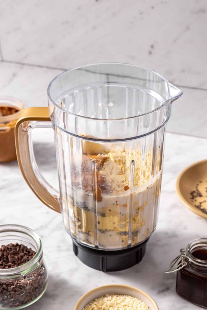 Side view of blender filled with banana, almond butter, and coconut milk for a healthy dessert smoothie