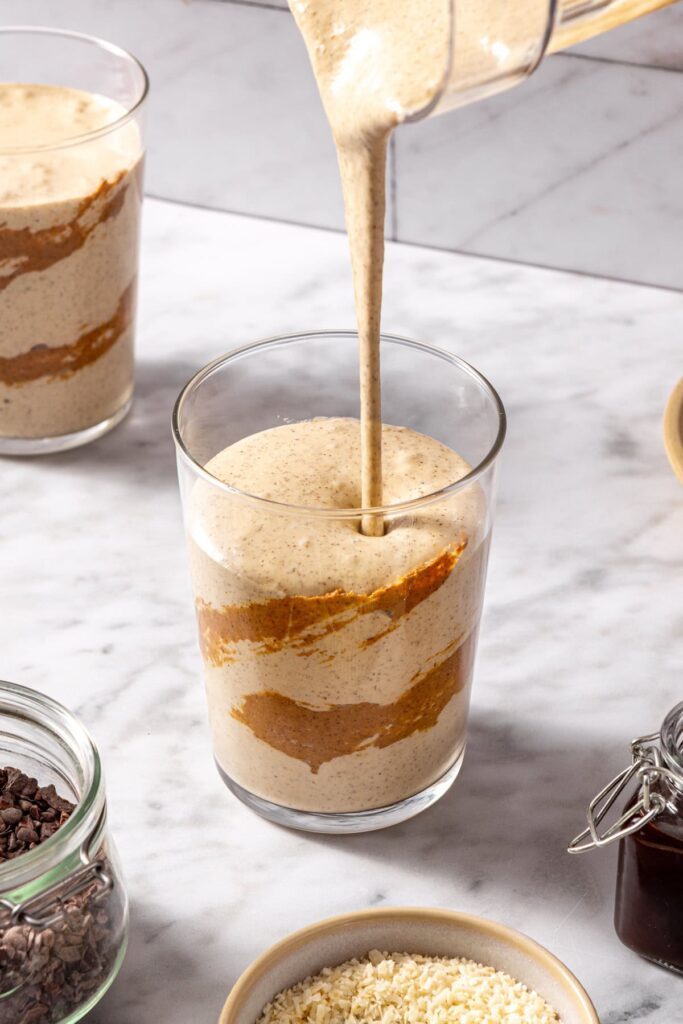 Pouring healthy dessert smoothie into glass with almond butter drizzle