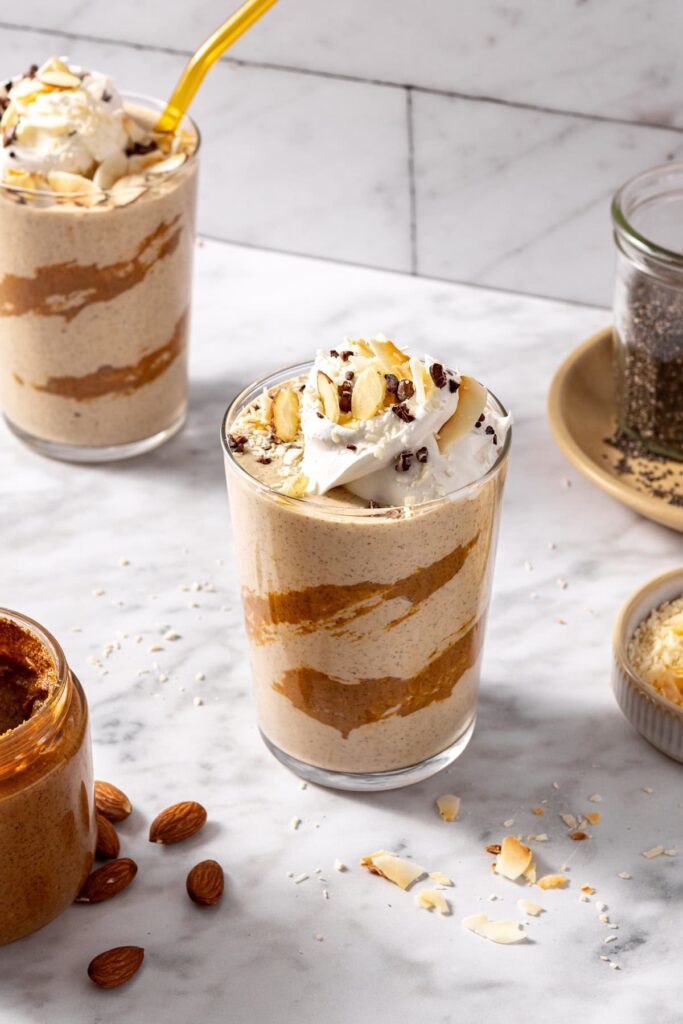 Healthy dessert smoothie in a glass topped with cacao nibs and coconut flakes on a styled table