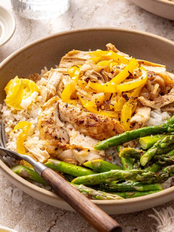 Cozy chicken thigh rice bowls with shredded chicken, asparagus, peppers and jasmine rice topped with ghee, close-up side angle