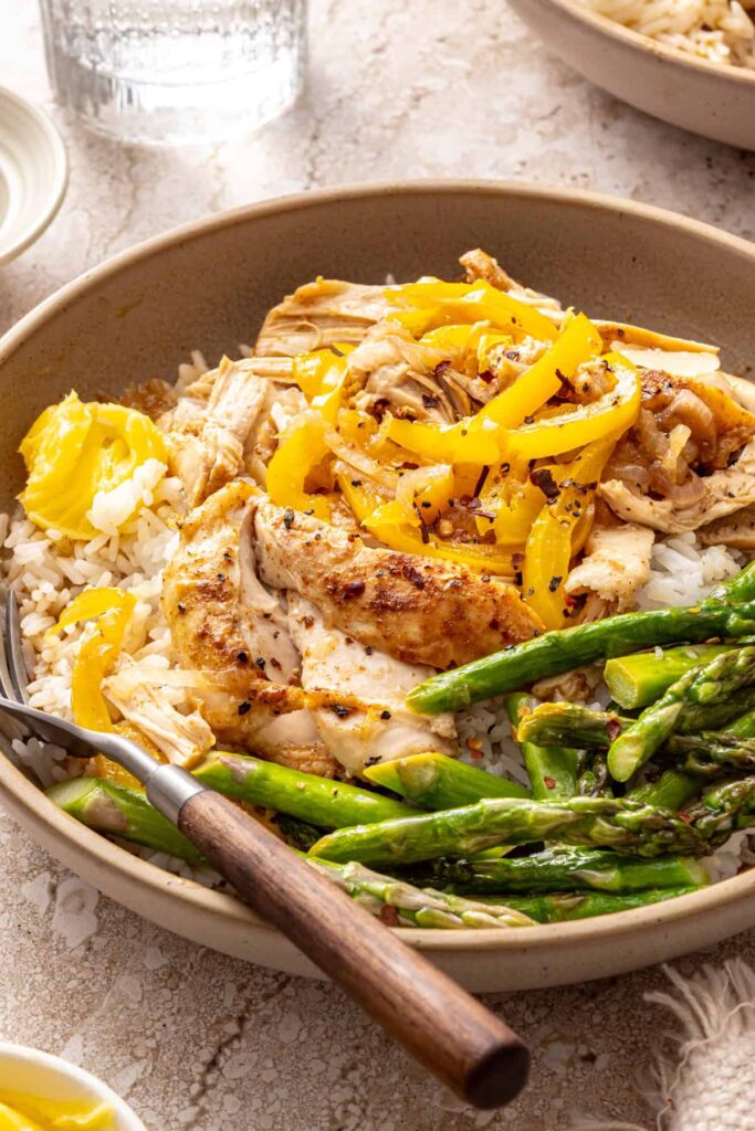 Cozy chicken thigh rice bowls with shredded chicken, asparagus, peppers and jasmine rice topped with ghee, close-up side angle