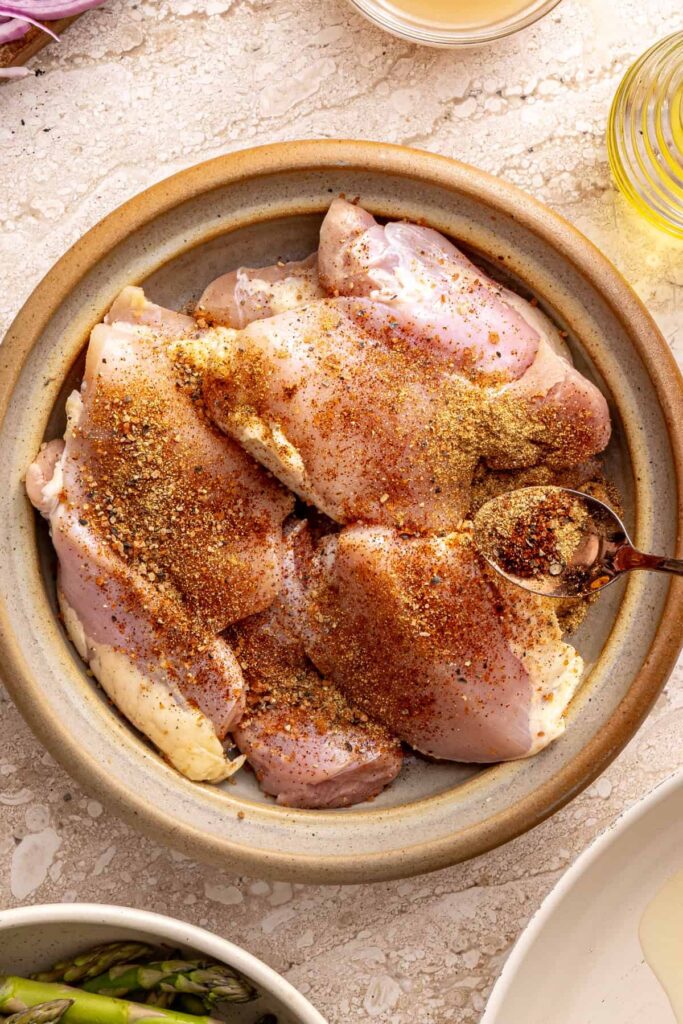 seasoning chicken thighs on a plate before searing for a cozy rice bowl recipe