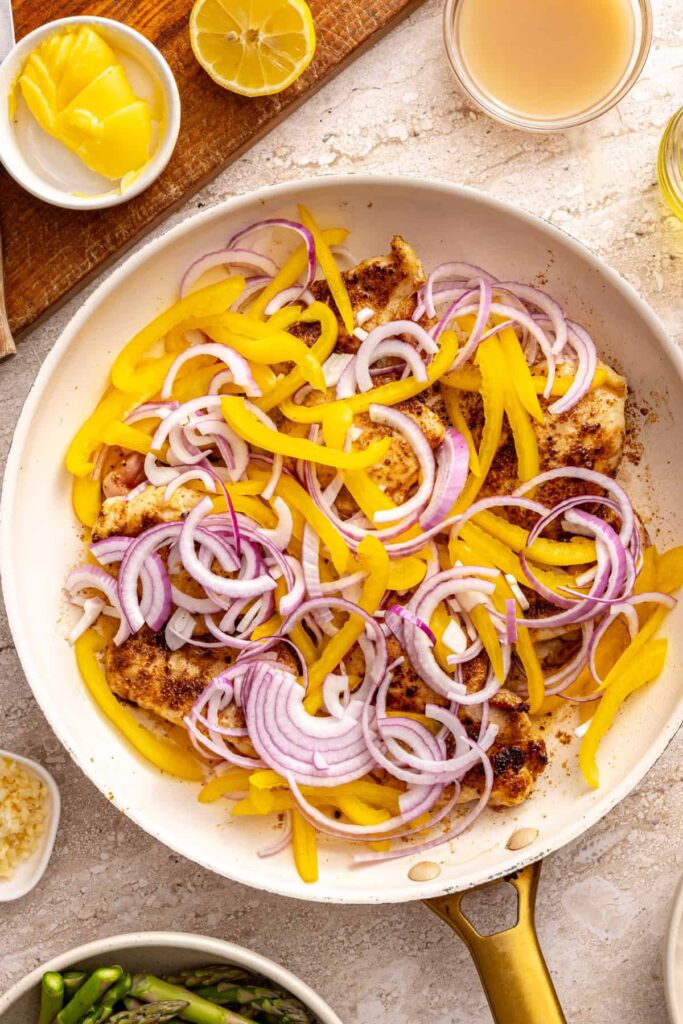 Adding sliced peppers and onion to chicken thighs in skillet
