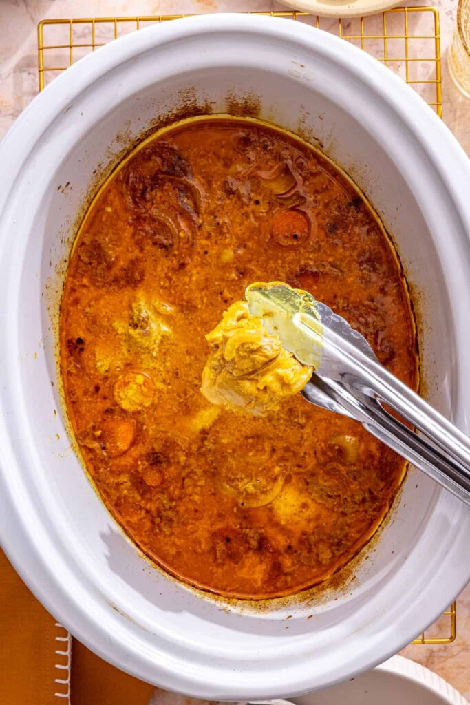 tongs removing chicken from slow cooker chicken curry, before shredding