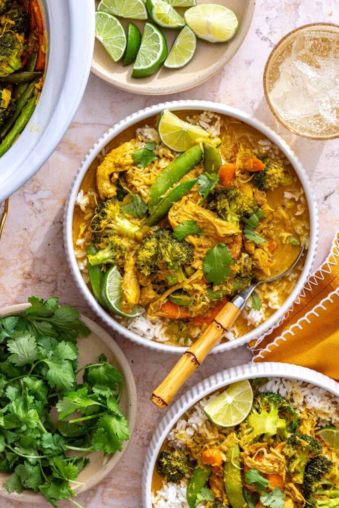 slow cooker chicken curry served over rice on styled table with cilantro and lime
