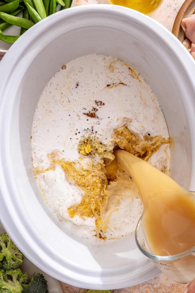 pouring bone broth and coconut milk into curry paste in slow cooker