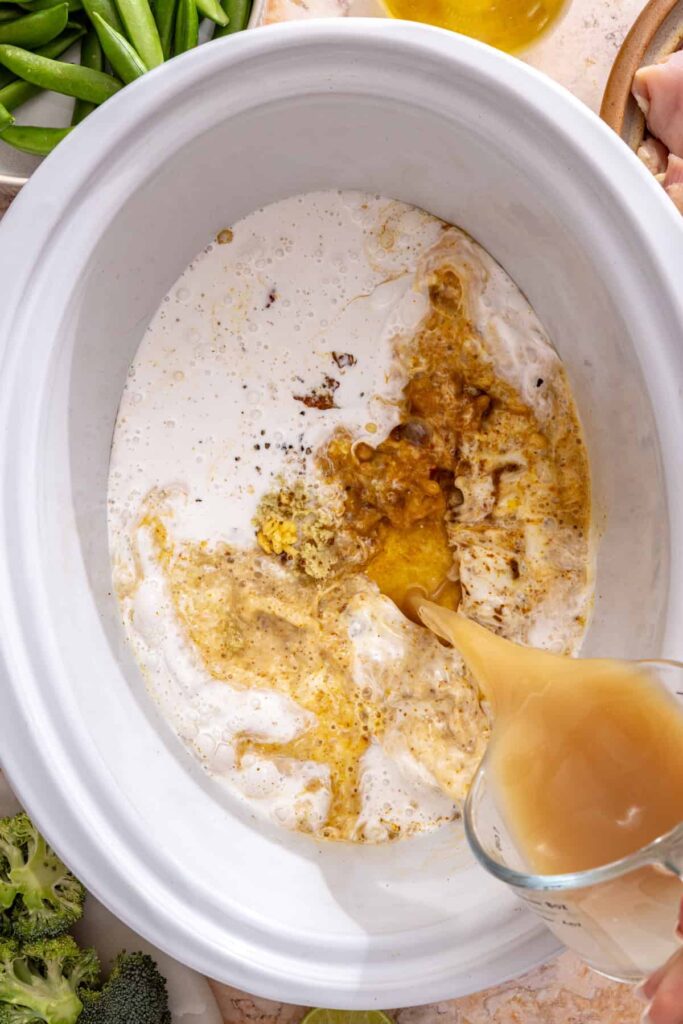 pouring bone broth and coconut milk into curry paste in slow cooker