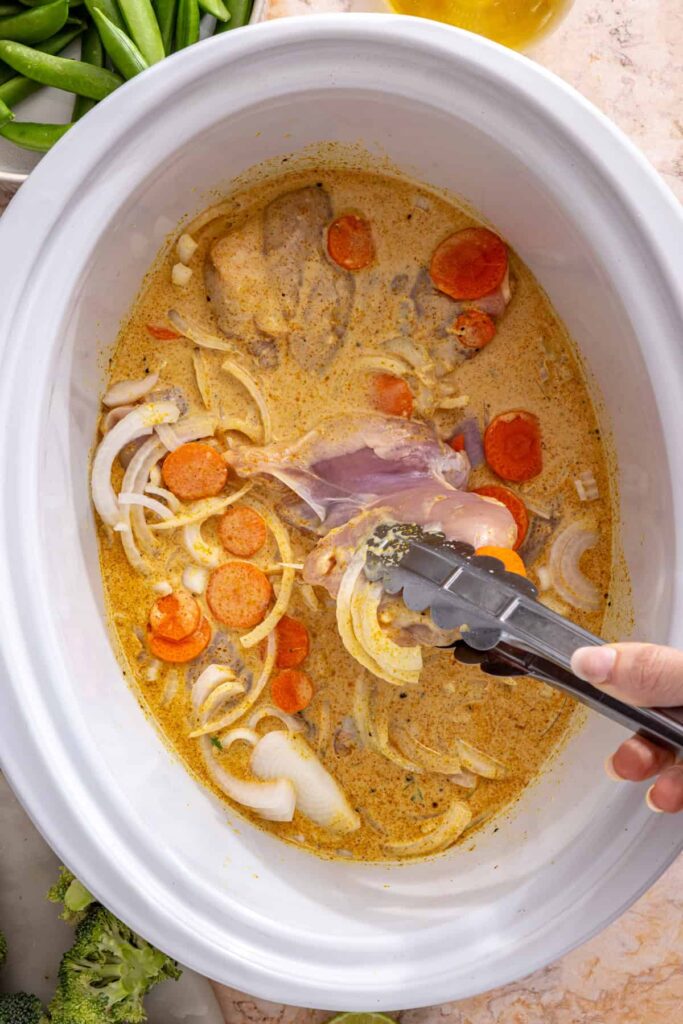 adding chicken thighs, carrots, and onions to slow cooker curry