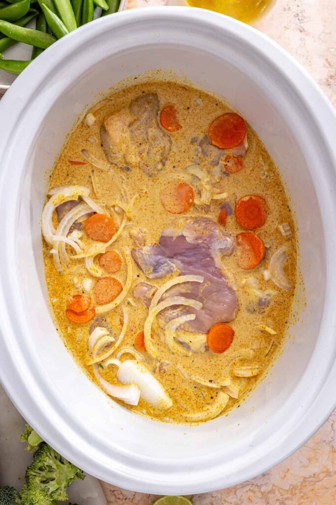 raw chicken and vegetables added to crockpot chicken curry base