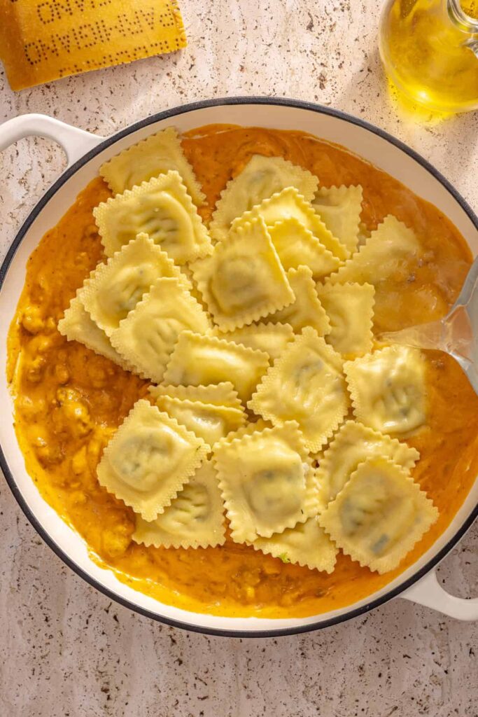 Mixing ravioli with creamy roasted vegetable sauce and reserved pasta water
