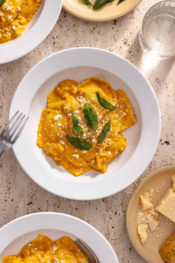 bowl of raviolis with hidden veggie sauce on a table styled with plate of fresh parm and glass of water nearby