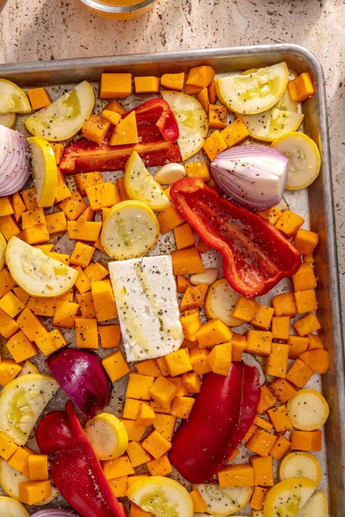 Sheet pan of veggies and feta ready to roast for creamy ravioli sauce