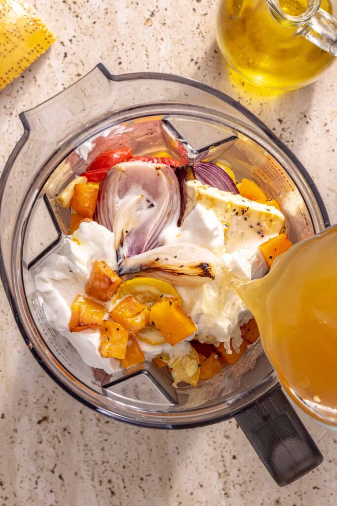 pouring bone broth for hidden veggie ravioli sauce into blender with chopped veggies and coconut cream