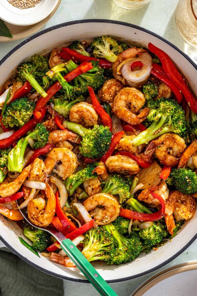 Overhead shot of shrimp stir fry in skillet with vegetables and sesame garnish