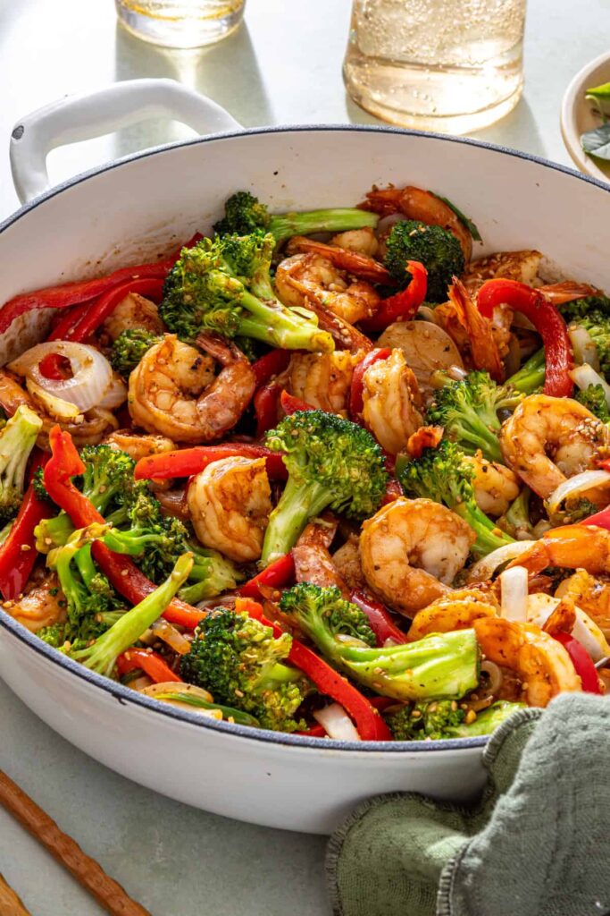 Styled shrimp stir fry scene with pan, chopsticks, and simple table setting
