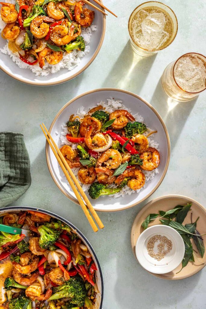 Shrimp stir fry served over rice with chopsticks on styled table