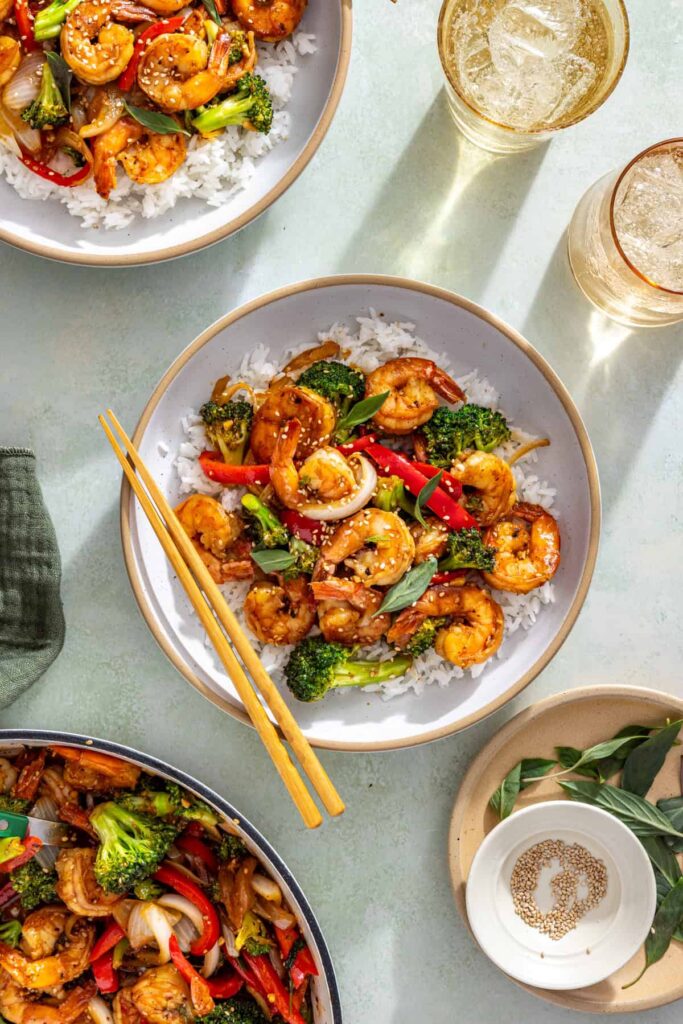 Overhead shrimp stir fry bowl with rice, sesame seeds, and basil