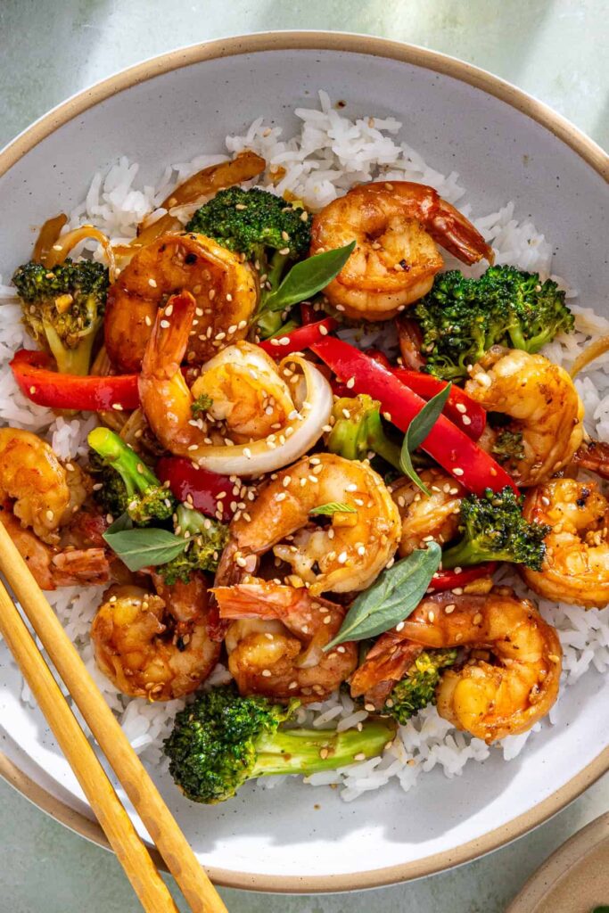 Overhead shrimp stir fry bowl with rice, sesame seeds, and basil