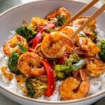 Easy shrimp stir fry served over rice with chopsticks lifting shrimp from bowl